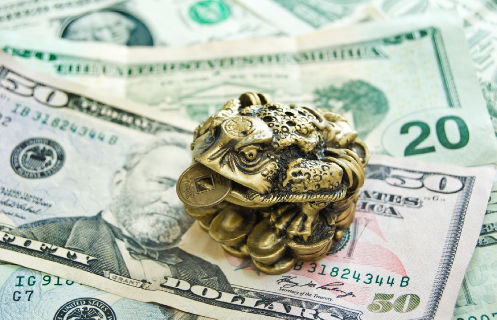 Сувенирная лягушка с монетой в руках сидит на денежных купюрах