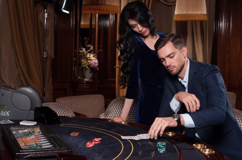 Сексуальная брюнетка поддерживает своего мужчину, играющего в покер в зале дорого казино