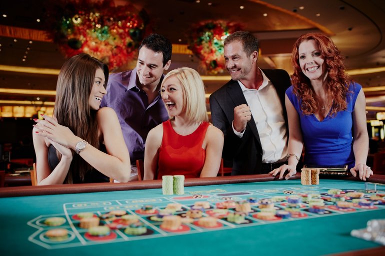 Блондинка, шатенка и рыжеволосая девушка веселятся за игрой в рулетку в компании двух симпатичных мужчин
