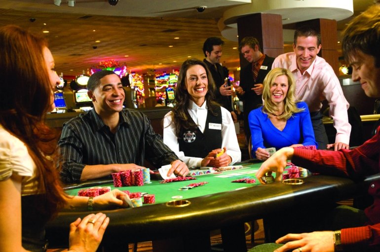 Молодая девушка крупье слушает игроков, сидя за столом для покера в зале дорогого казино