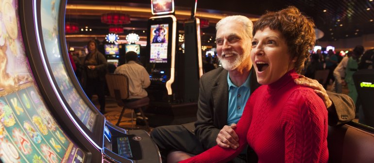 Женщина и мужчина зрелого возраста восторженно кричат, смотря на экран игрового автомата