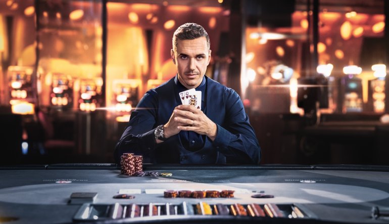 Серьезный мужчина в дорогой одежде сидит за игорным столом с парой карт в руках