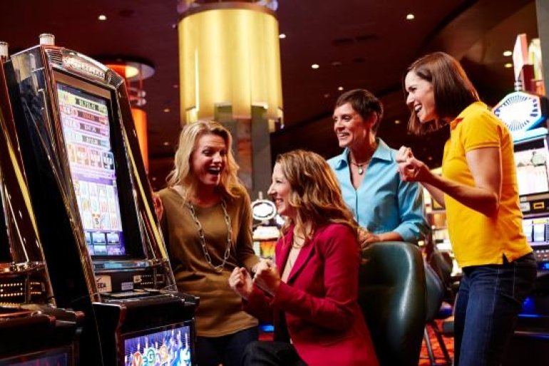 Три симпатичных молодых женщины и мужчина за игрой на автомате в казино